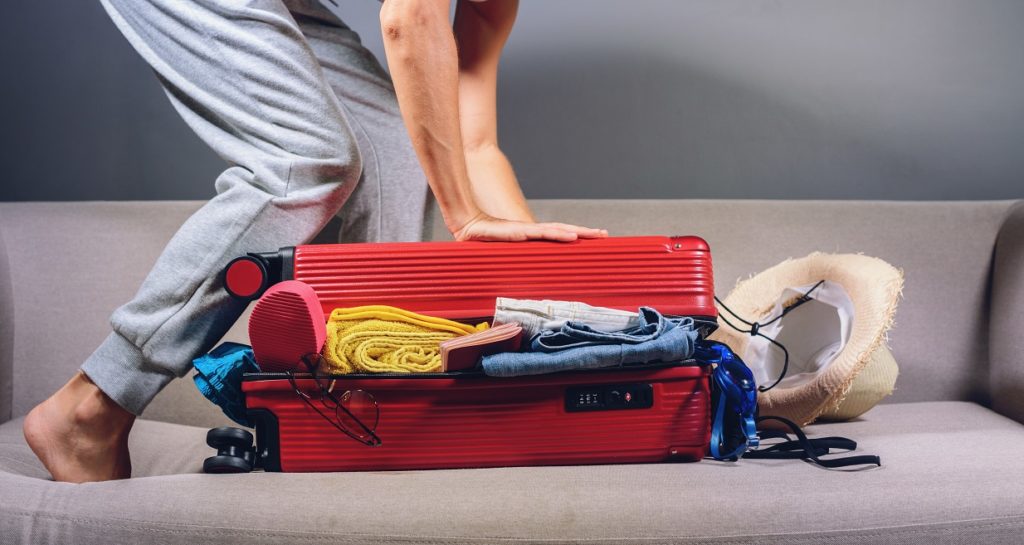 woman packing red suitcase to travel in coronaviru H77U8J5