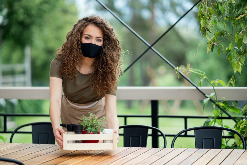 Waitress with face mask working outdoors on terrace restaurant