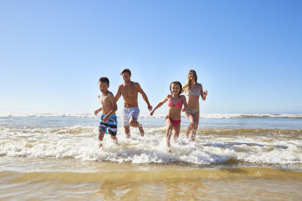 Family On Summer Beach Vacation Run Out Of Sea Towards Camera